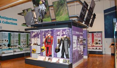 A glazed exhibition space showing racing gear worn by the face road motorbike racer Joey Dunlop