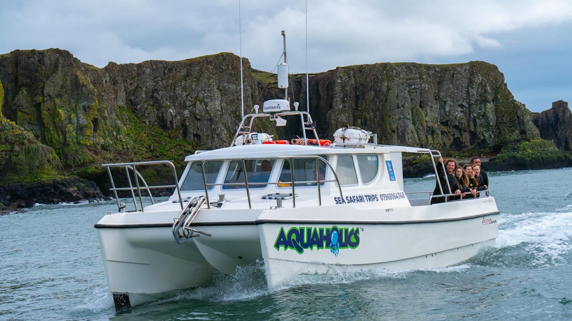 Aquaholics dive boat travelling along the Causeway Coast with cliffs in the background and passengers on board, viewed from the water. Aquaholics dive boat travelling along the Causeway Coast with cliffs in the background and passengers on board, viewed from the water.