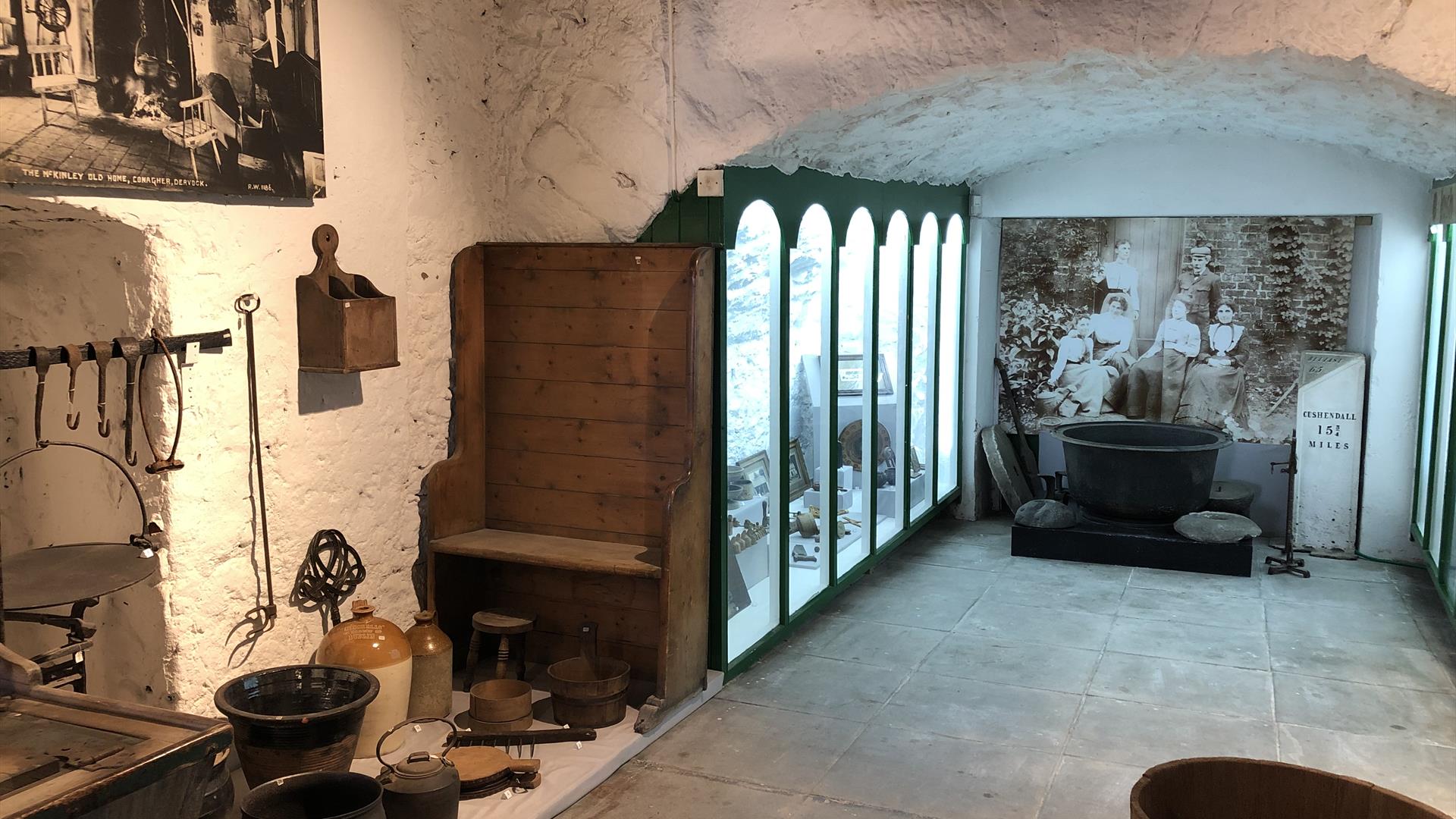 inside view of exhibits in museum looking down a passageway with some items attached to wall, some on floor, and a glass fronted display case on left.