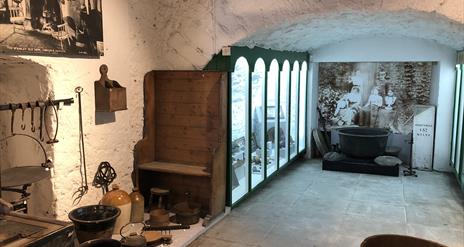 inside view of exhibits in museum looking down a passageway with some items attached to wall, some on floor, and a glass fronted display case on left.