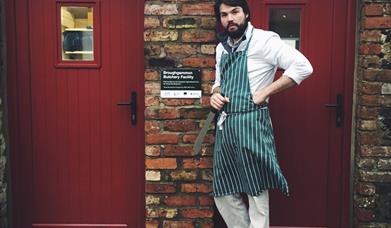 Man wearing an apron standing outside the butchery facility with a knife ready to work