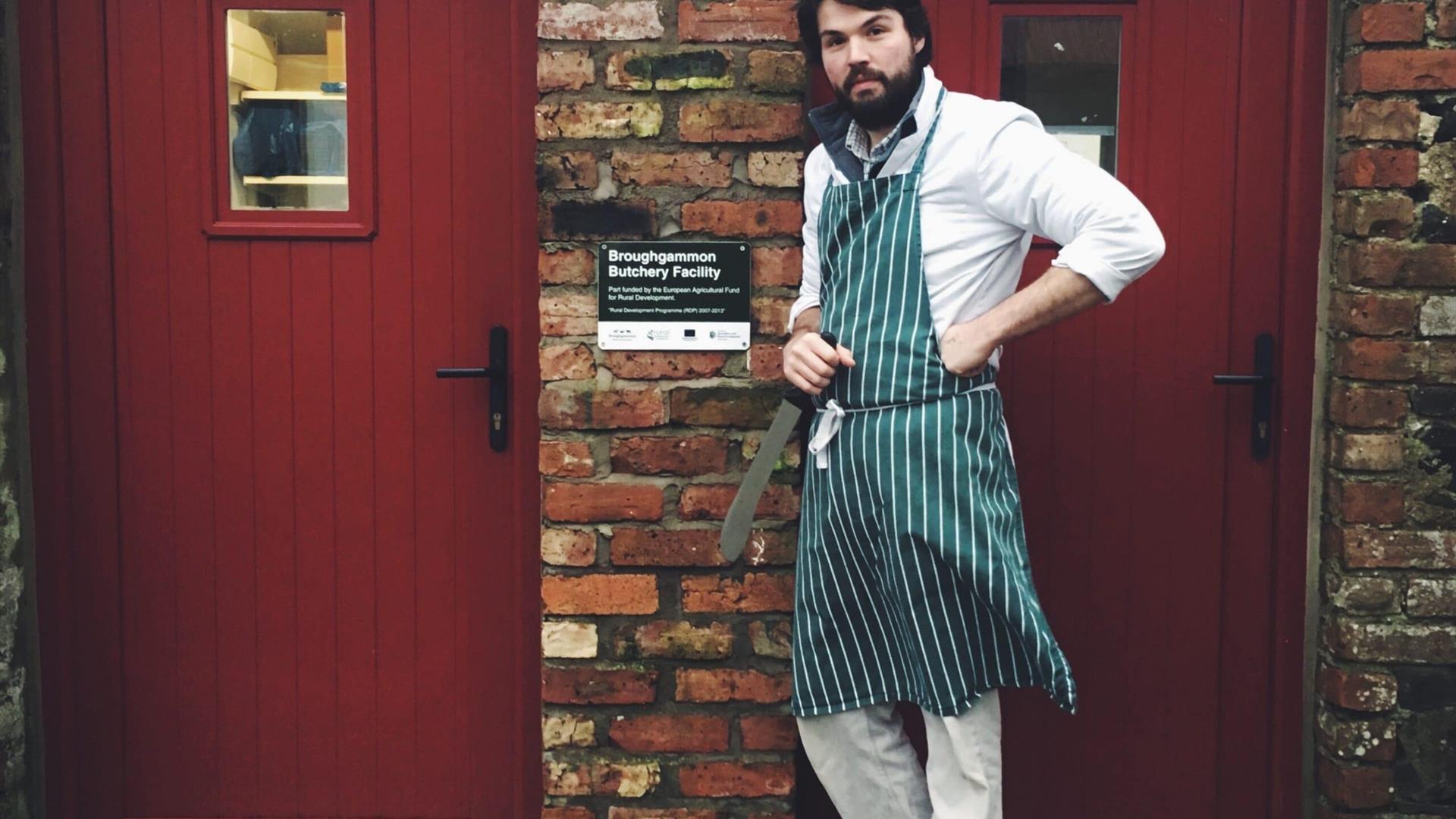 Man wearing an apron standing outside the butchery facility with a knife ready to work