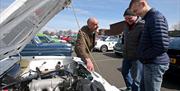 Three men looking under the bonnet of a while vehicle at the vintage car display