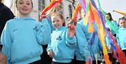 Dancers with blue jumpers twirling brightly coloured material as they make their way through the parade