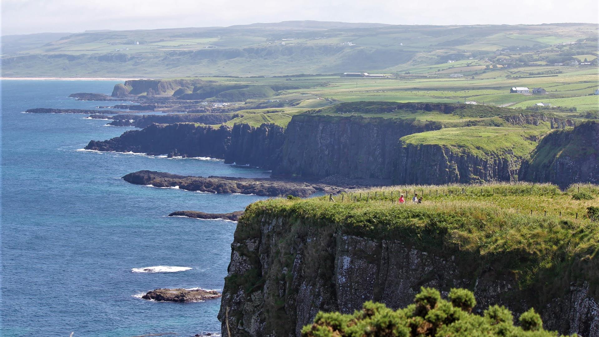 people walking a top a cliff with the sea below