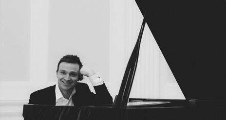 black and white image of Cahal Masterson sitting at a grand piano smiling.
