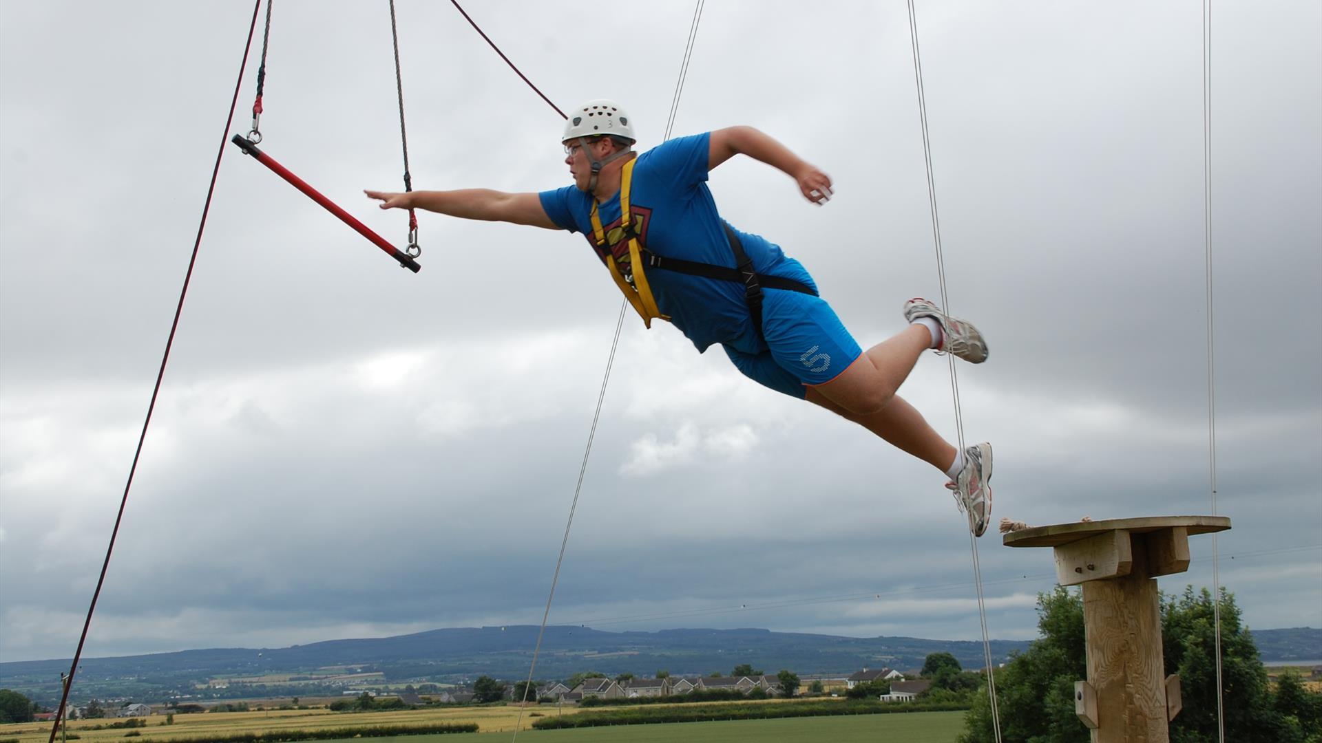 A man in a blue t-shirt reaching out for high ropes