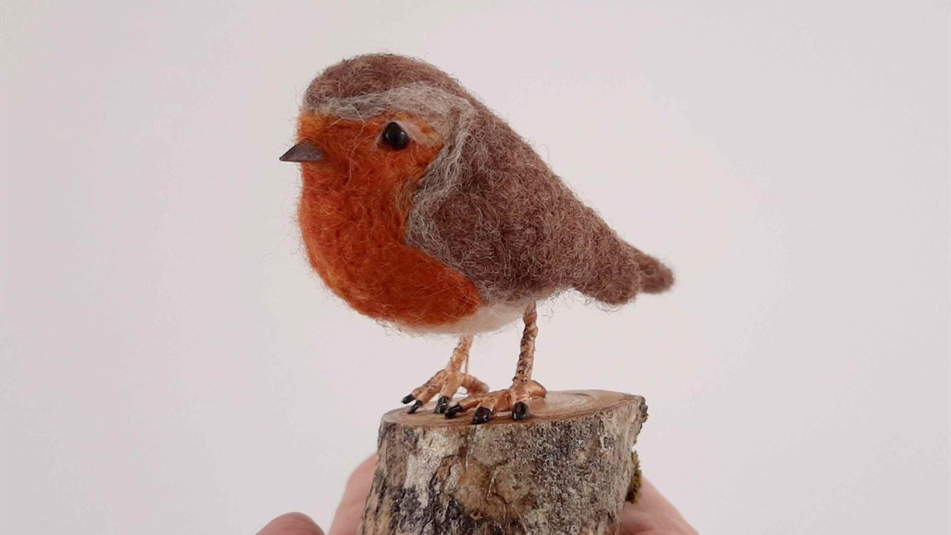 a person's hand holds a wool felted sculpture of a robin bird on a small articifical tree stump a person's hand holds a wool felted sculpture of a robin bird on a small articifical tree stump