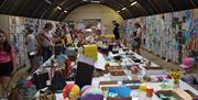 a table filled with art materials and displays and walls either side displaying art and posters at the Ballymoney Show