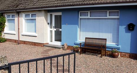 Picture depicting the external view of No.$ self-catering. A blue semi-detached house with white windows and door fronted by a gravel yard and blue ga