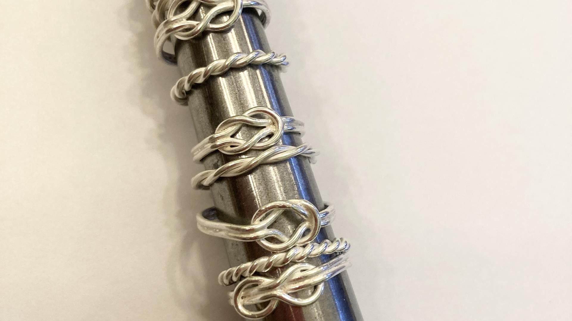 a selection of handmade silver rings in the shape of knots on a ring sizer. a selection of handmade silver rings in the shape of knots on a ring sizer.