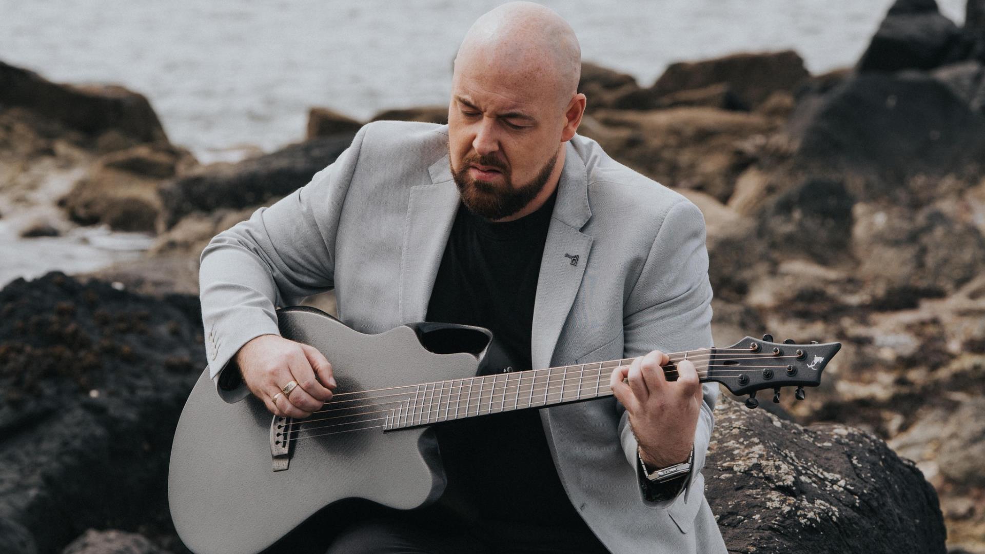 musician Jamie Sloan strums a guitar while sitting outside on coastal rocks musician Jamie Sloan strums a guitar while sitting outside on coastal rocks