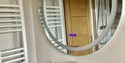 bathroom with modern washbasin and hanging large round mirror and heated towel rail