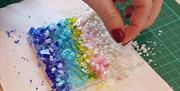 a person's hand adds colourful crushed glass to their artwork