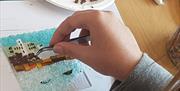 a person's hand uses tweezers to add small pieces of glass to their artwork