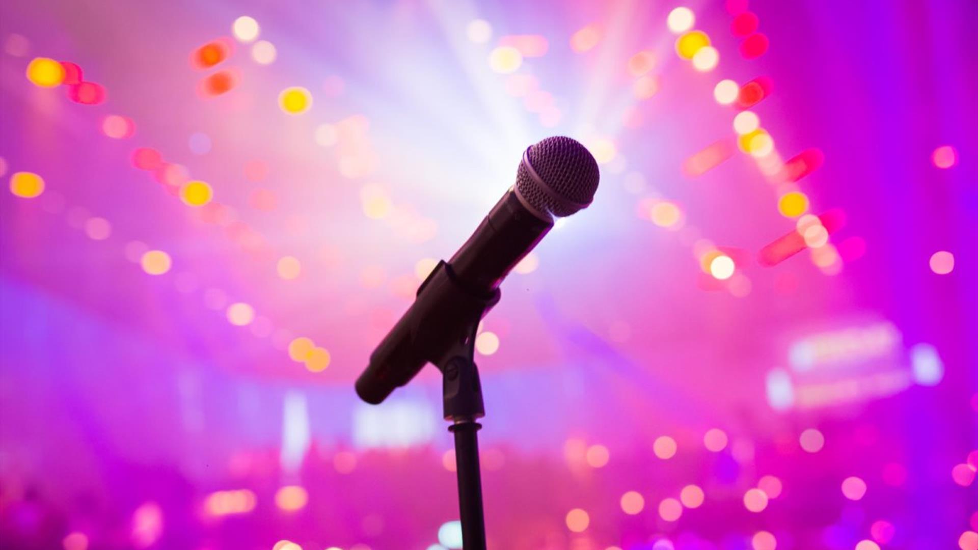 Microphone on a stand against a pink backdrop illuminated with lights Microphone on a stand against a pink backdrop illuminated with lights