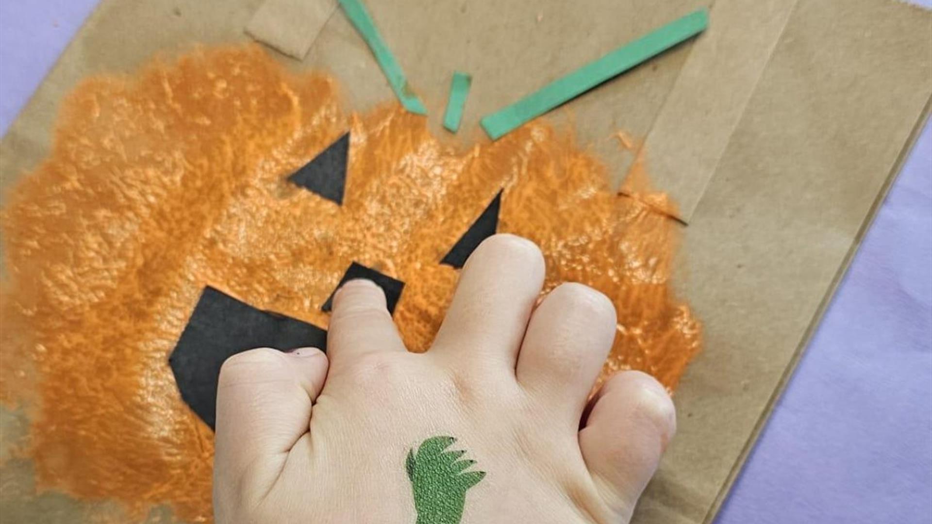 a child's hand is placed on a pumpkin which has been painted onto a brown paper bag a child's hand is placed on a pumpkin which has been painted onto a brown paper bag