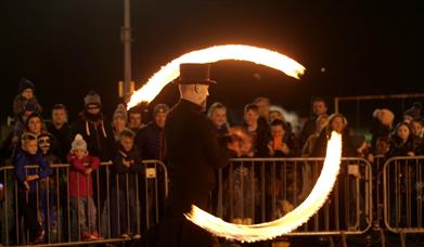 Image shows a man with fire poi entertaining the crowd