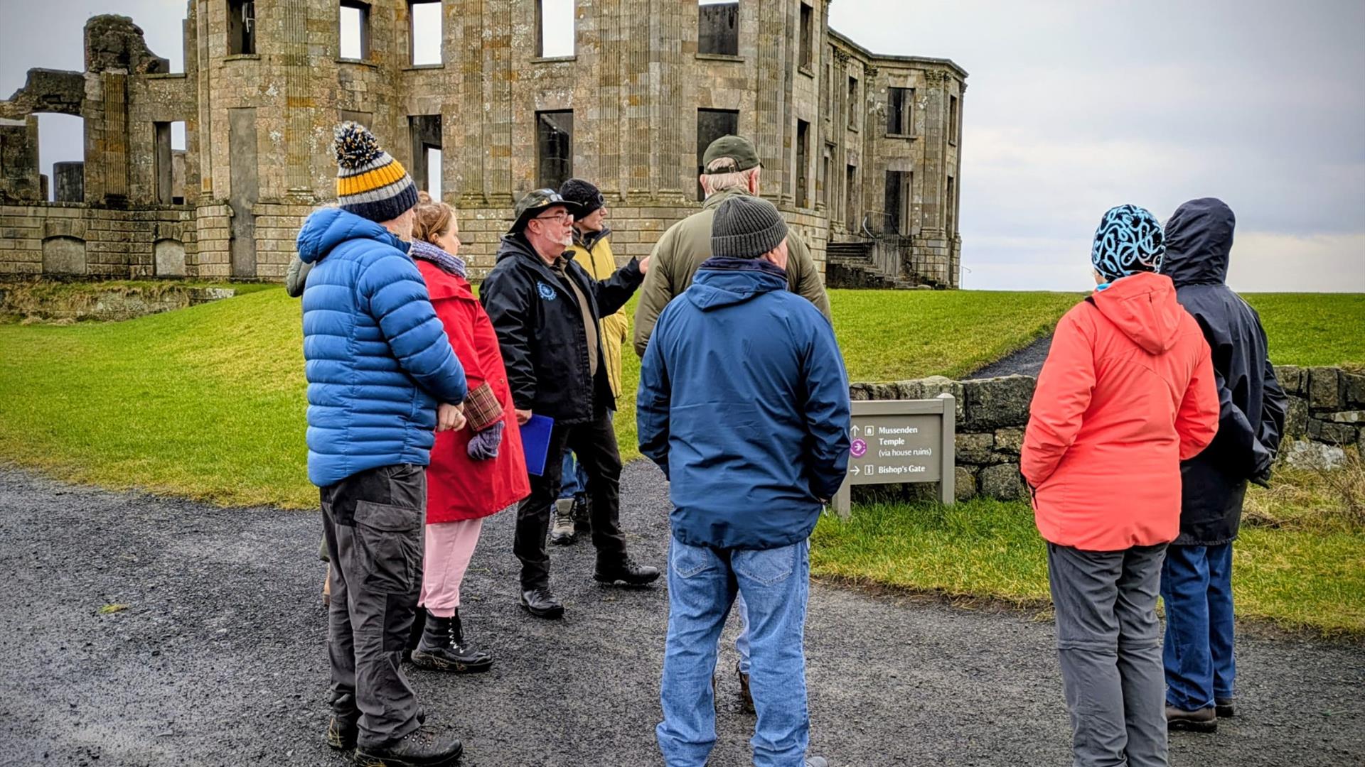 Bob Picken guiding a group in outdoor clothing while looking at the ruins on the Downhill Demesne Bob Picken guiding a group in outdoor clothing while looking at the ruins on the Downhill Demesne