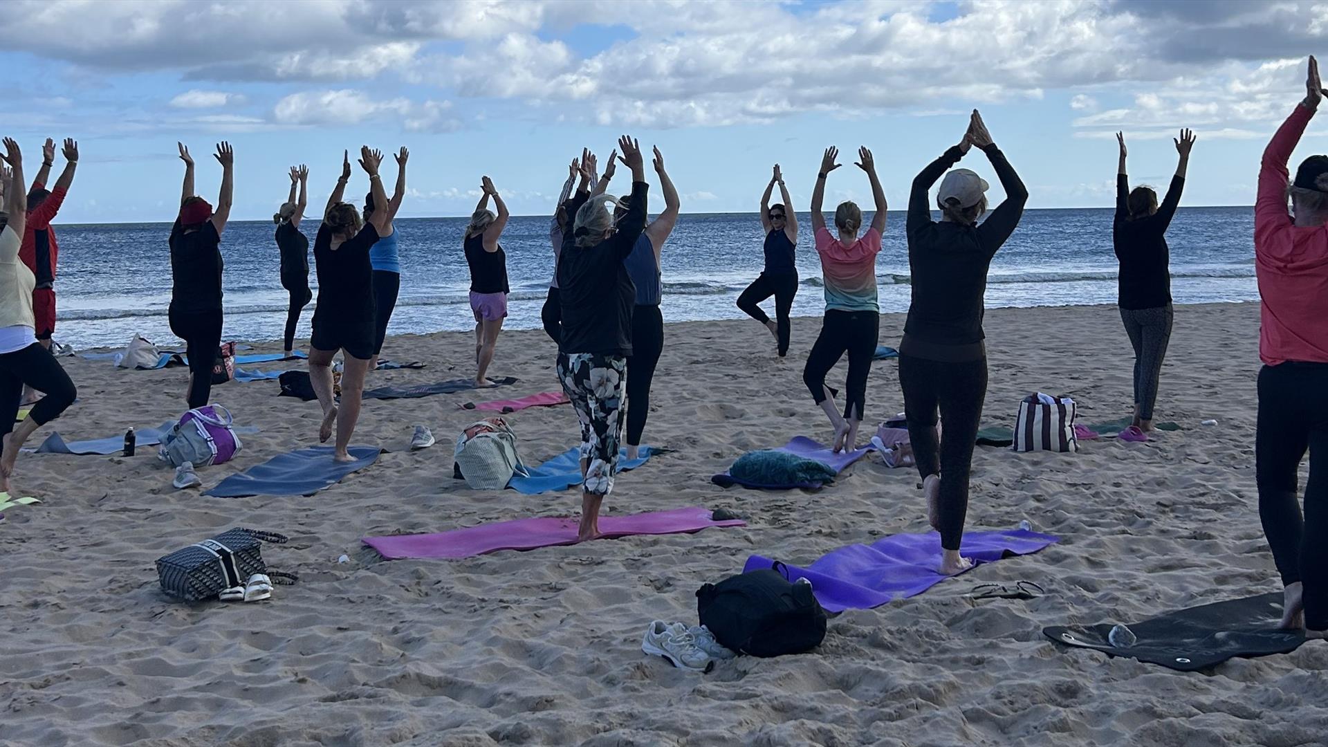 a group of people doing yoga stretches on a beach a group of people doing yoga stretches on a beach
