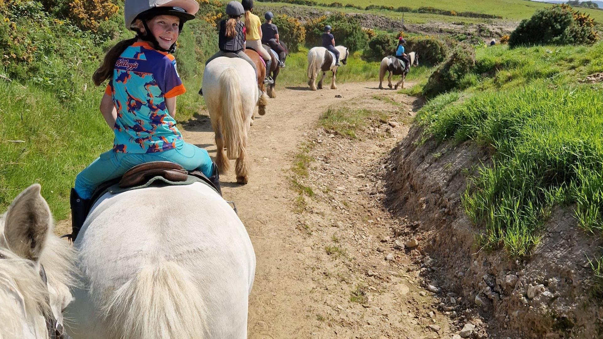 a group of children and adults are riding on horseback through the countryside