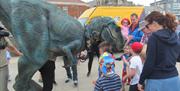 Image shows a large mechanical dinosaur with a group of children standing round it.