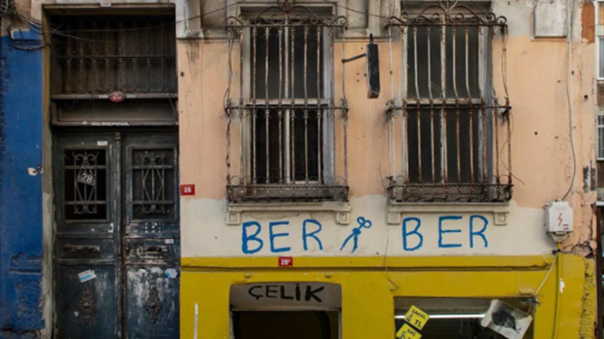 A rundown looking building housing a barber shop with graffiti saying 'Ber Ber' and a pair of scissors