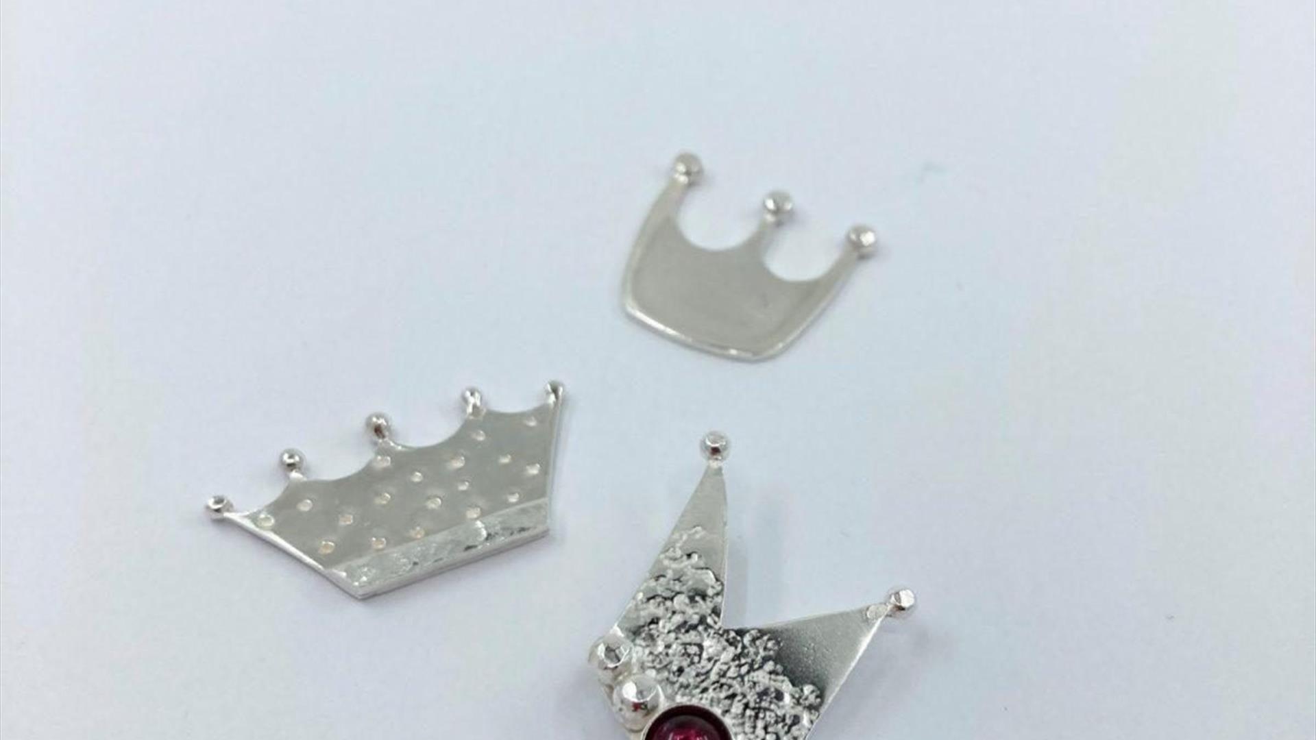 Image shows 3 crowns made from silver,  they vary in size and the largest one has a red jewel in the middle.