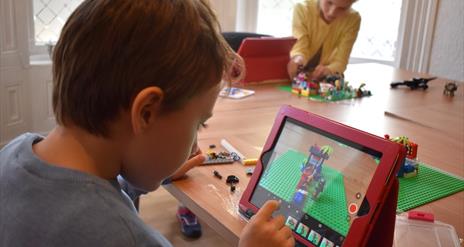 Picture of a child sitting with an iPad in front of a Lego scene