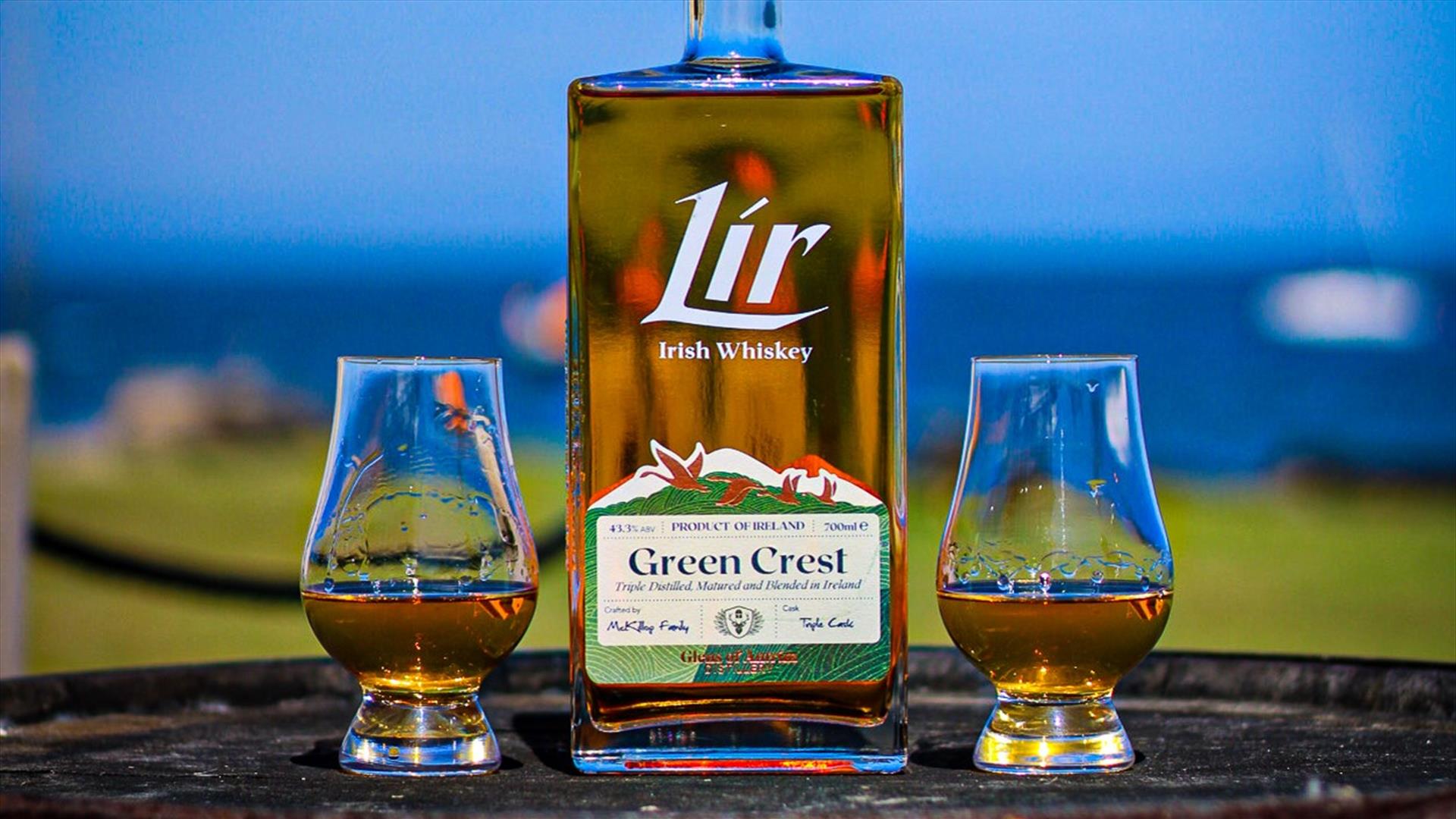A bottle of Lir Irish Whiskey and 2 filled glasses sitting on a barrel