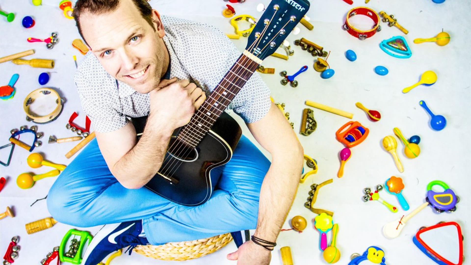 kyle riley surrounded by children's instruments, holding a guitar kyle riley surrounded by children's instruments, holding a guitar