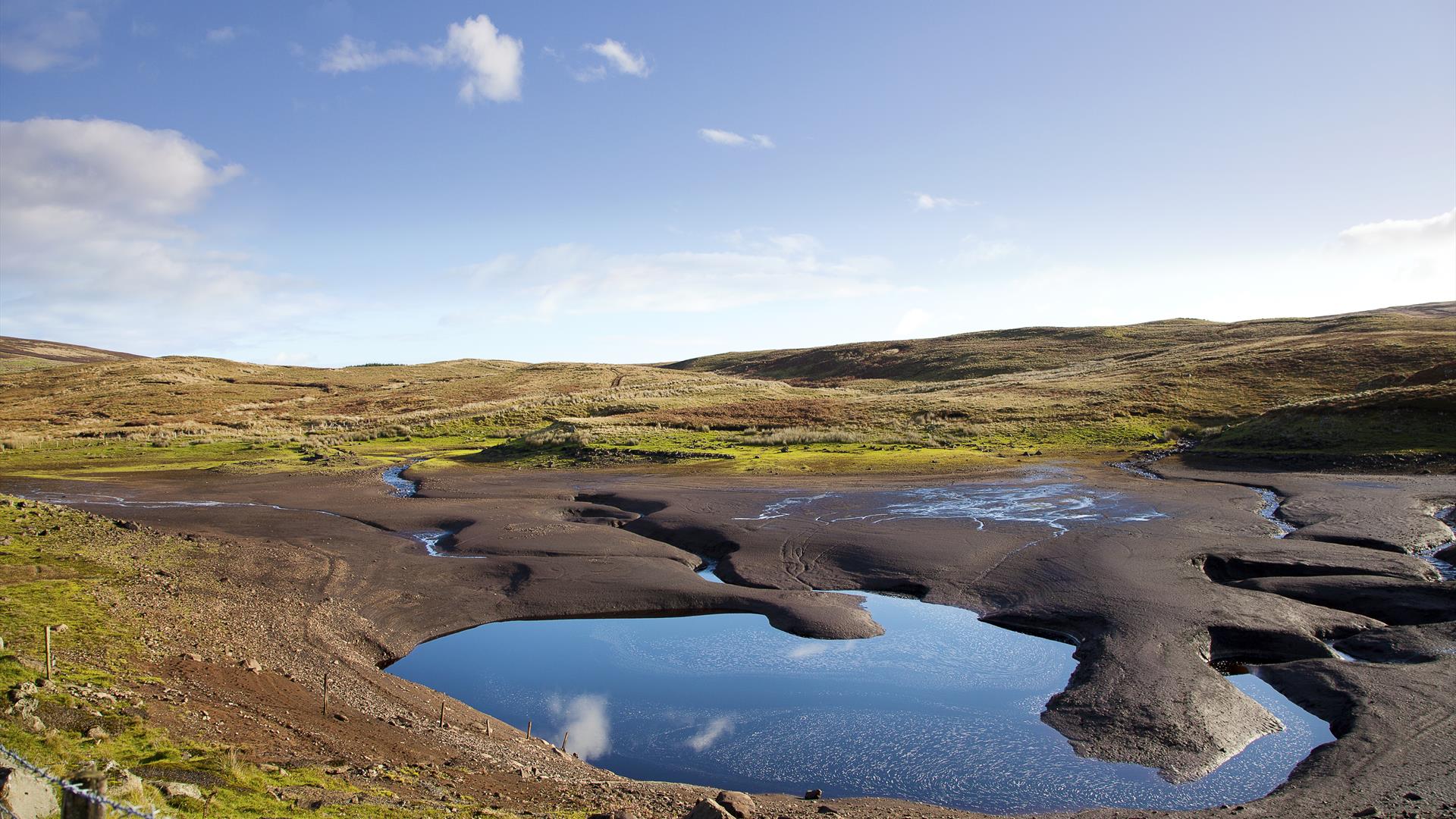 close up of the clear water known as "the vanishing lake" in Loughareema, County Antrim with the green countryside surrounding it and blue sky in dist close up of the clear water known as "the vanishing lake" in Loughareema, County Antrim with the green countryside surrounding it and blue sky in dist
