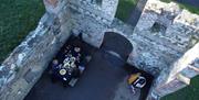 Aeriel shot of a group of people dining around a table in old castle ruins - there is no roof to the castle so the shot from above is unique. A harpis