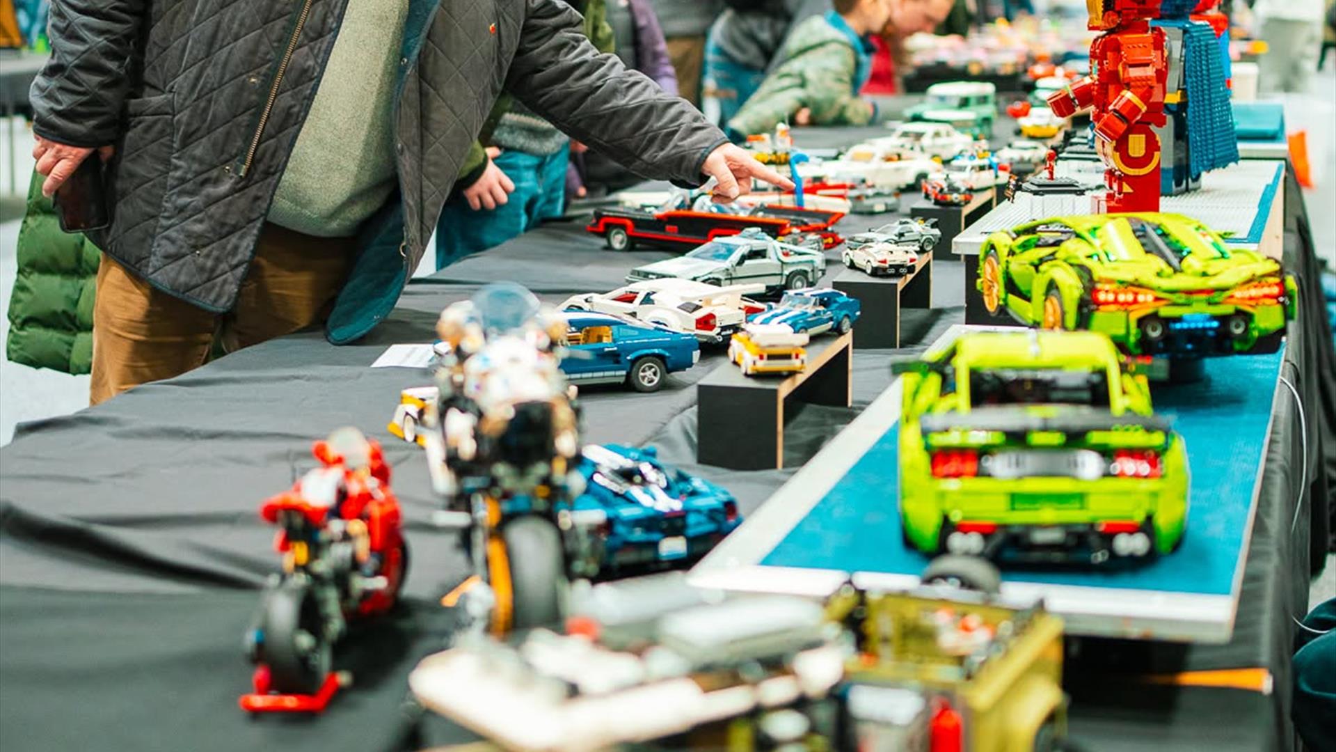people examining various tables and rows of lego sculptures people examining various tables and rows of lego sculptures