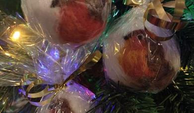 Image shows a needle felted robin decoration hanging on a Christmas tree