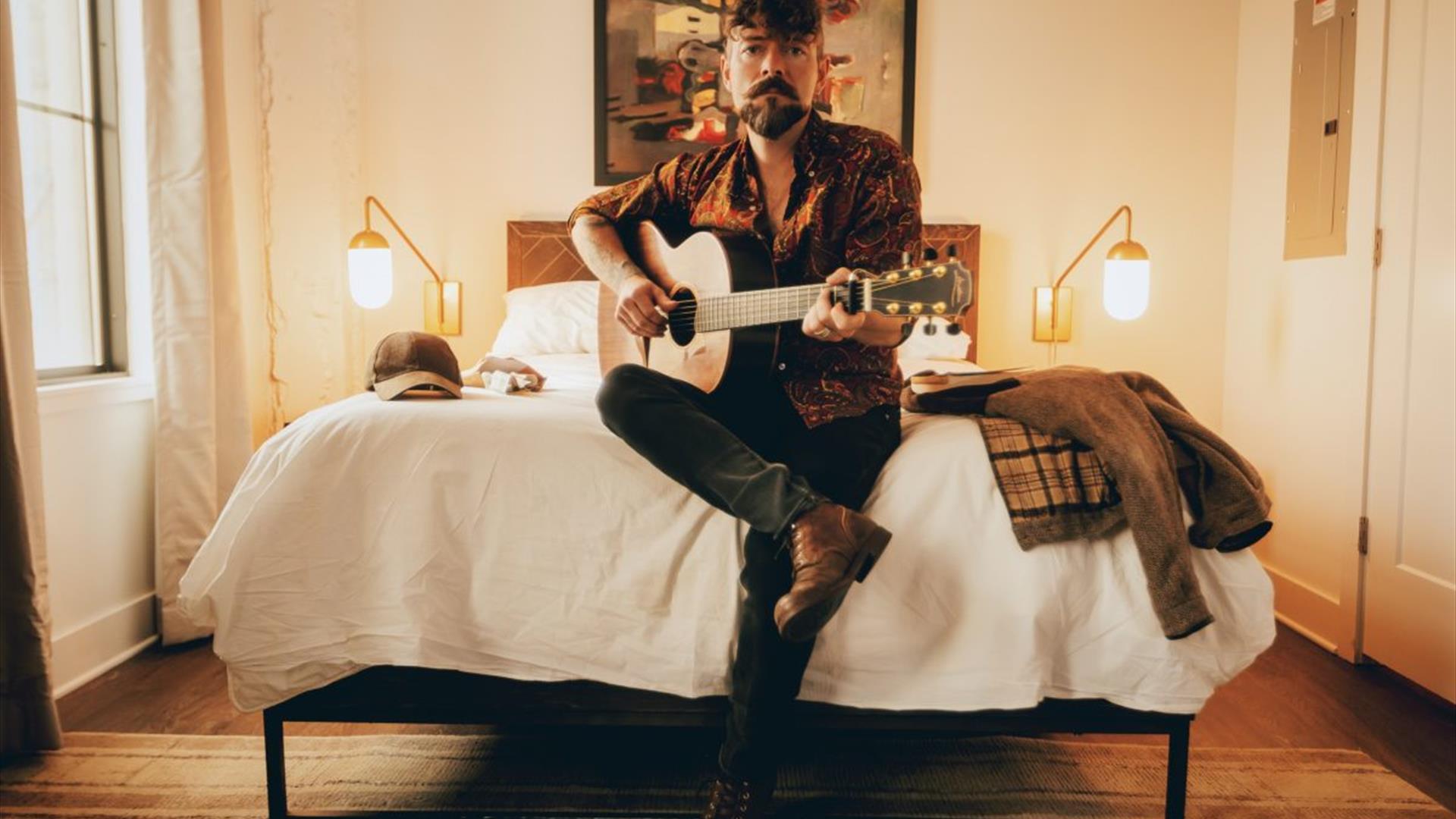 Singer Niall McCabe sits on the end of a double bed while holding an acoustic guitar and looking directly at the camera Singer Niall McCabe sits on the end of a double bed while holding an acoustic guitar and looking directly at the camera