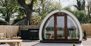 Exterior view of Glamping Pod with hot tub in background and picnic table to the front of the garden area.