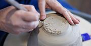 Patricia's hands use a sharp tool to sculpt the buttom of a ceramic piece