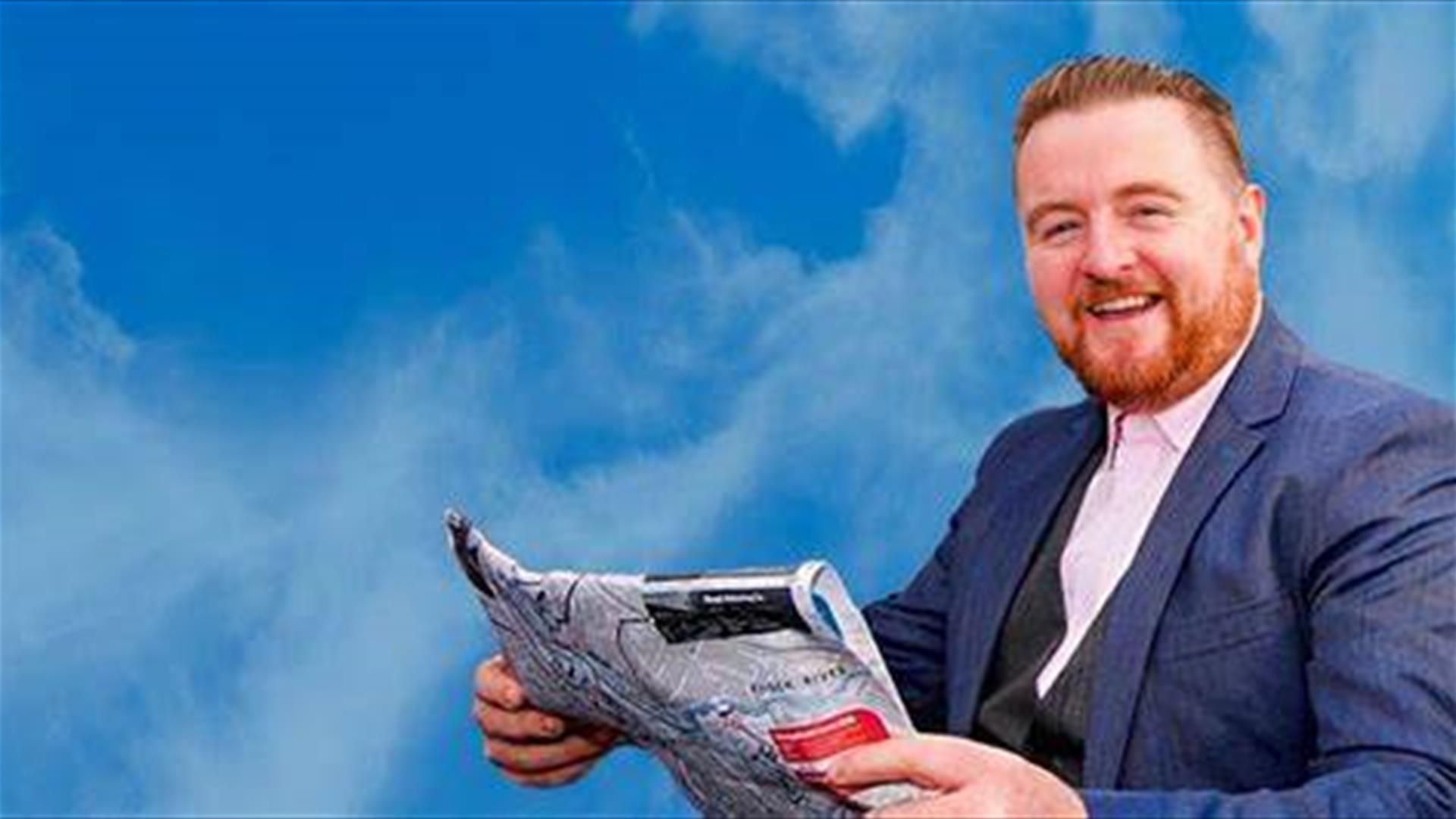 Image shows a man with a beard, wearing a suit and holding a newspaper