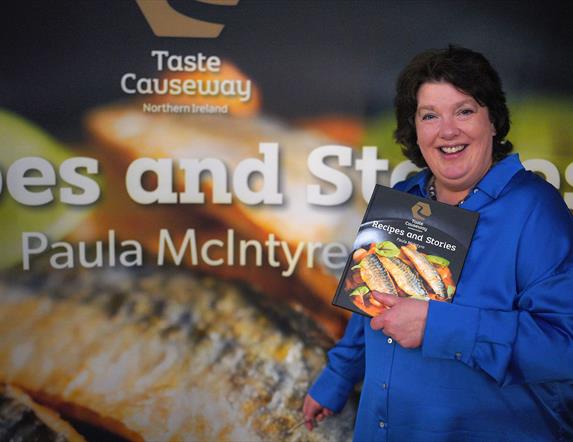 paula mcintyre holding a copy of the book "Recipes and Stories"