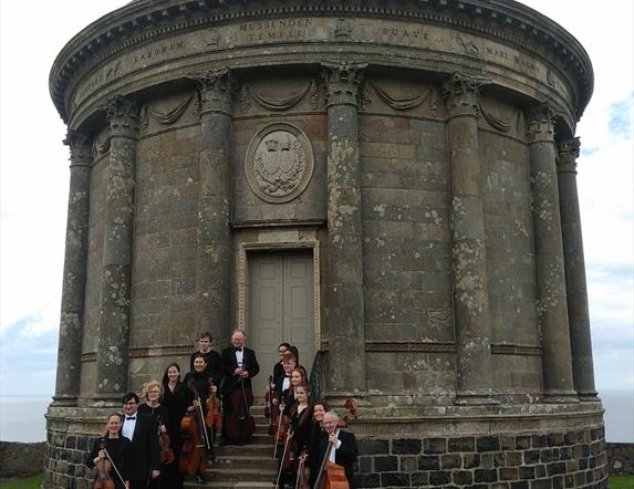 Donegal Chamber Orchestra pictured with their instruments standing on the steps of the Mussenden Temple