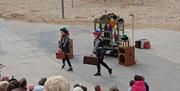 Two female performers wearing coloured hats and carrying suitcases entertain the crowds in Portstewart