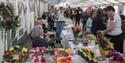 Crowds in a marquee looking at floral arrangements on a table covered with a white tablecloth