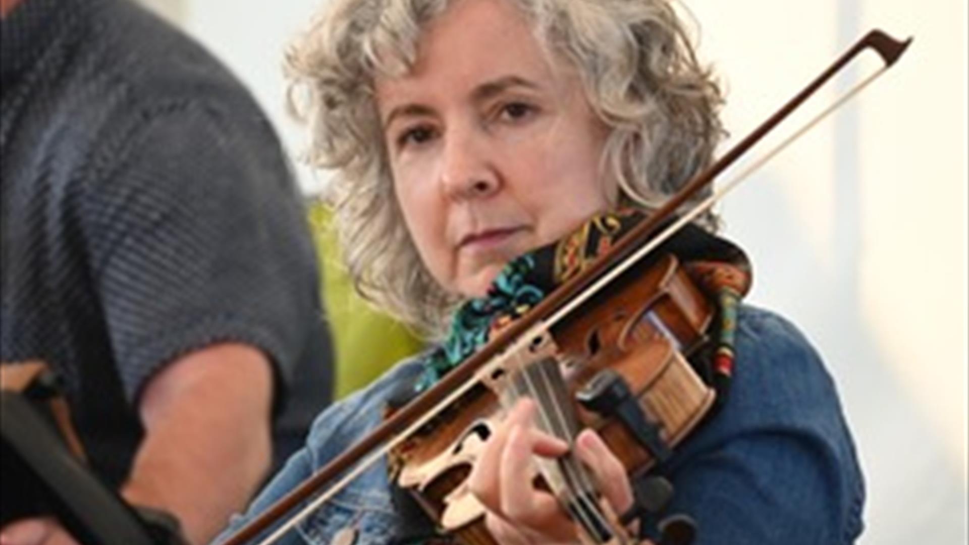Image shows lady playing the fiddle.  She is wearing a navy blue top and has short grey hair.