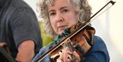 Image shows lady playing the fiddle.  She is wearing a navy blue top and has short grey hair.