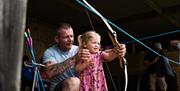 A man helping a young girl pull back the archery bow