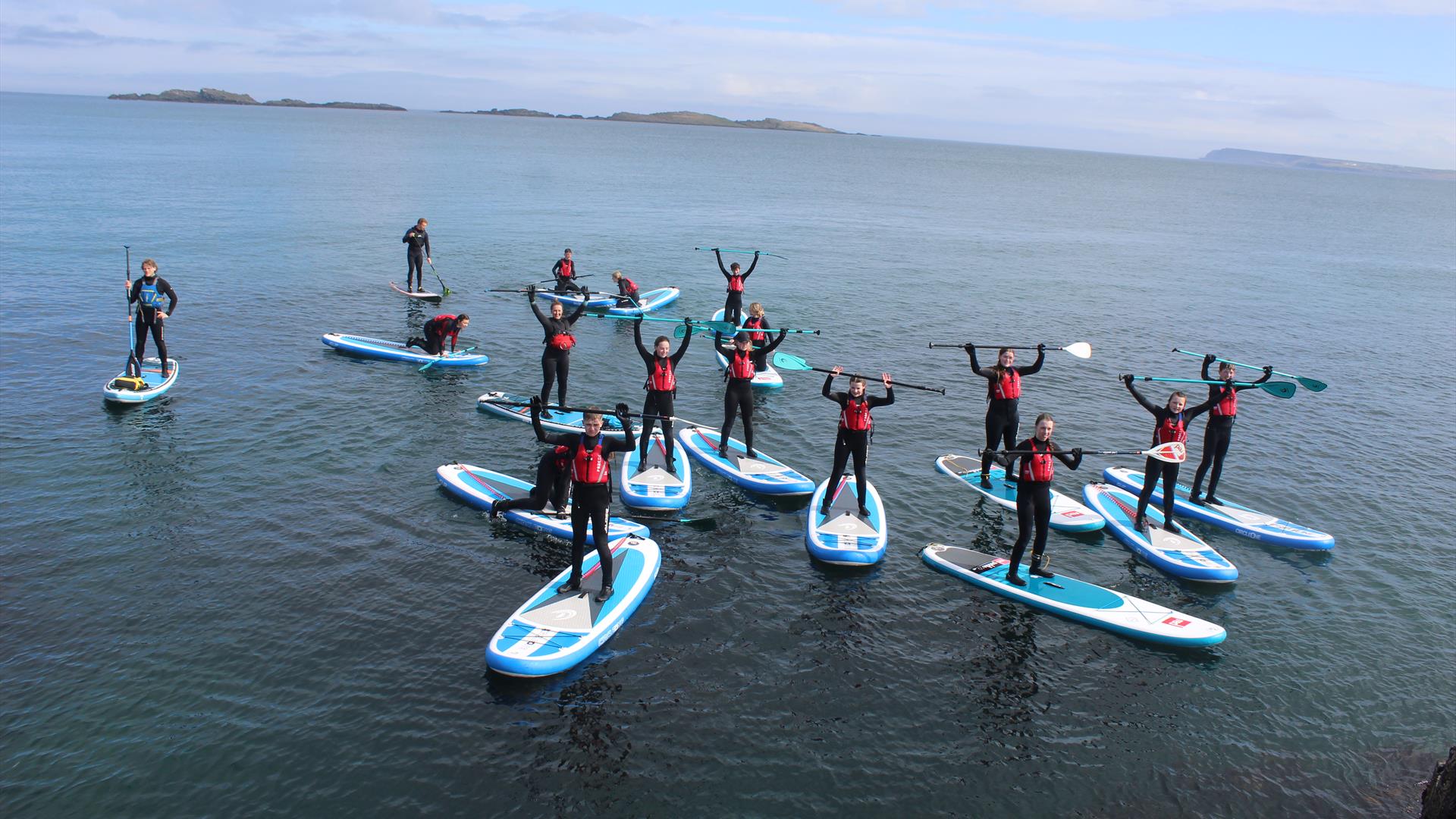 Group of older children and adults standing on paddleboards at sea with paddles raised