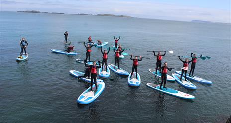 Group of older children and adults standing on paddleboards at sea with paddles raised