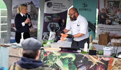 A cookery demonstration with a male chef showing salmon and a woman commentating to the crowd