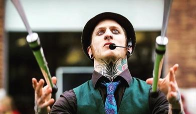 A man wearing a black hat and a blue tie juggling knives